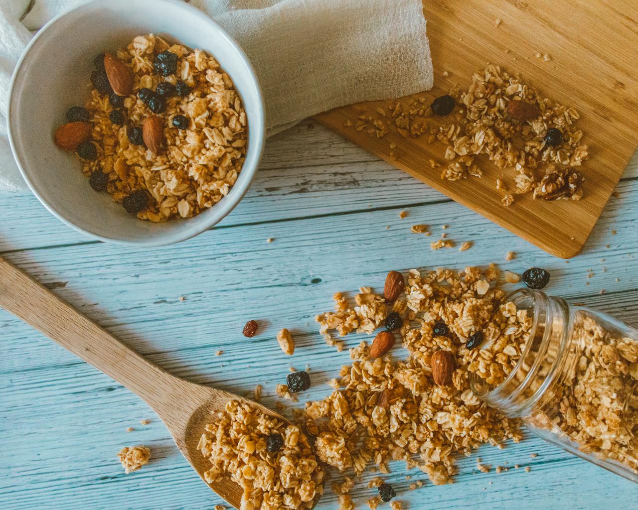 Top view of granola with almonds and berries spilled from a jar onto a wooden table.